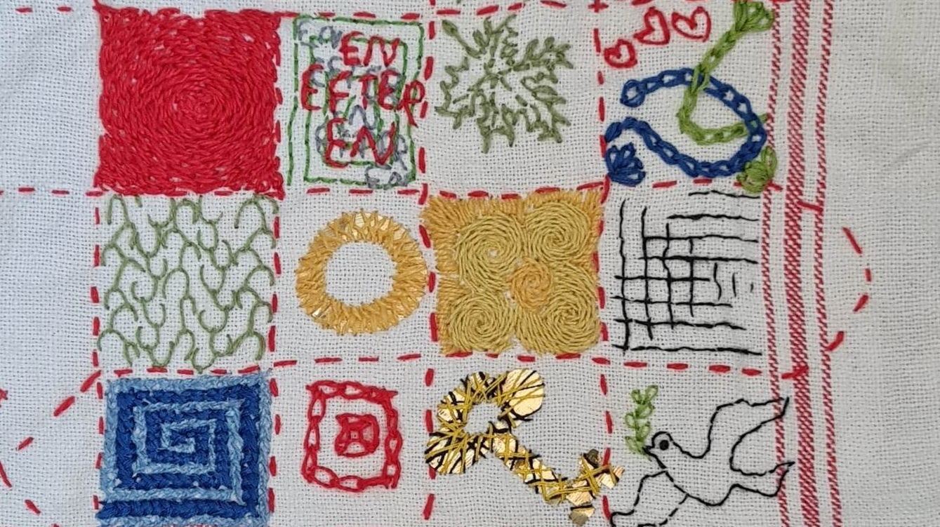 Boroderibingo. Broderier med olika teman fyller små rutor på en sliten linnehandduk