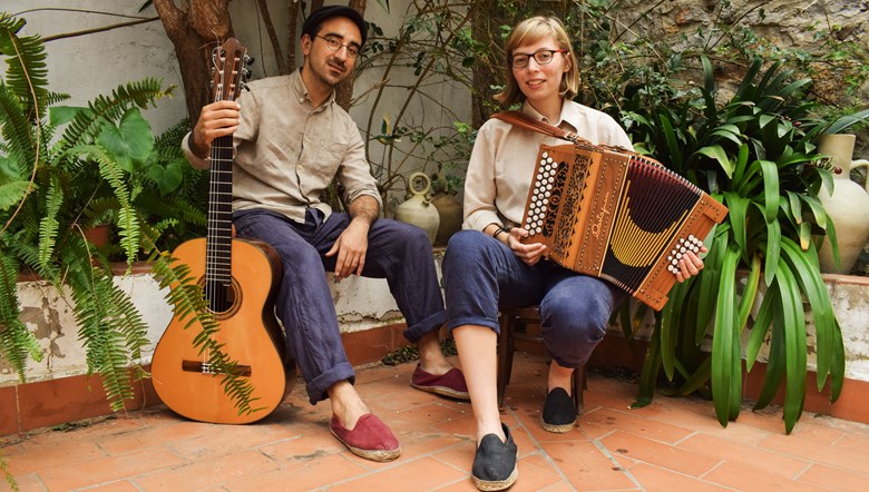 En man och en kvinna sitter bland gröna växter. Mannen håller en gitarr, kvinnan håller ett durspel. 