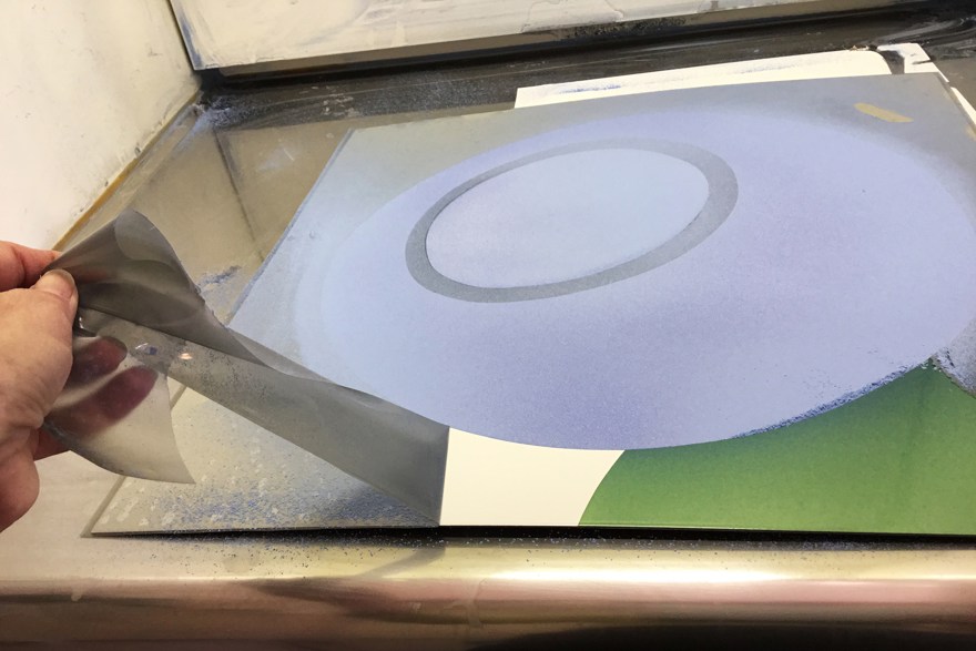 Marie Isaksson drar bort plastfilm från sprutmålad emaljplåt.