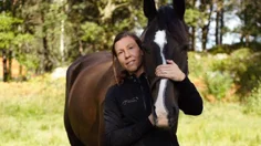 Porträtt på Nina Magnusson som står och håller händerna på en häst