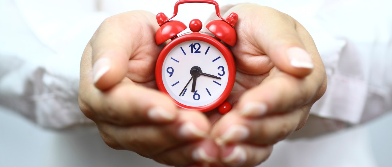 Närbild på två händer som håller i en röd, gammaldags väckarklocka.