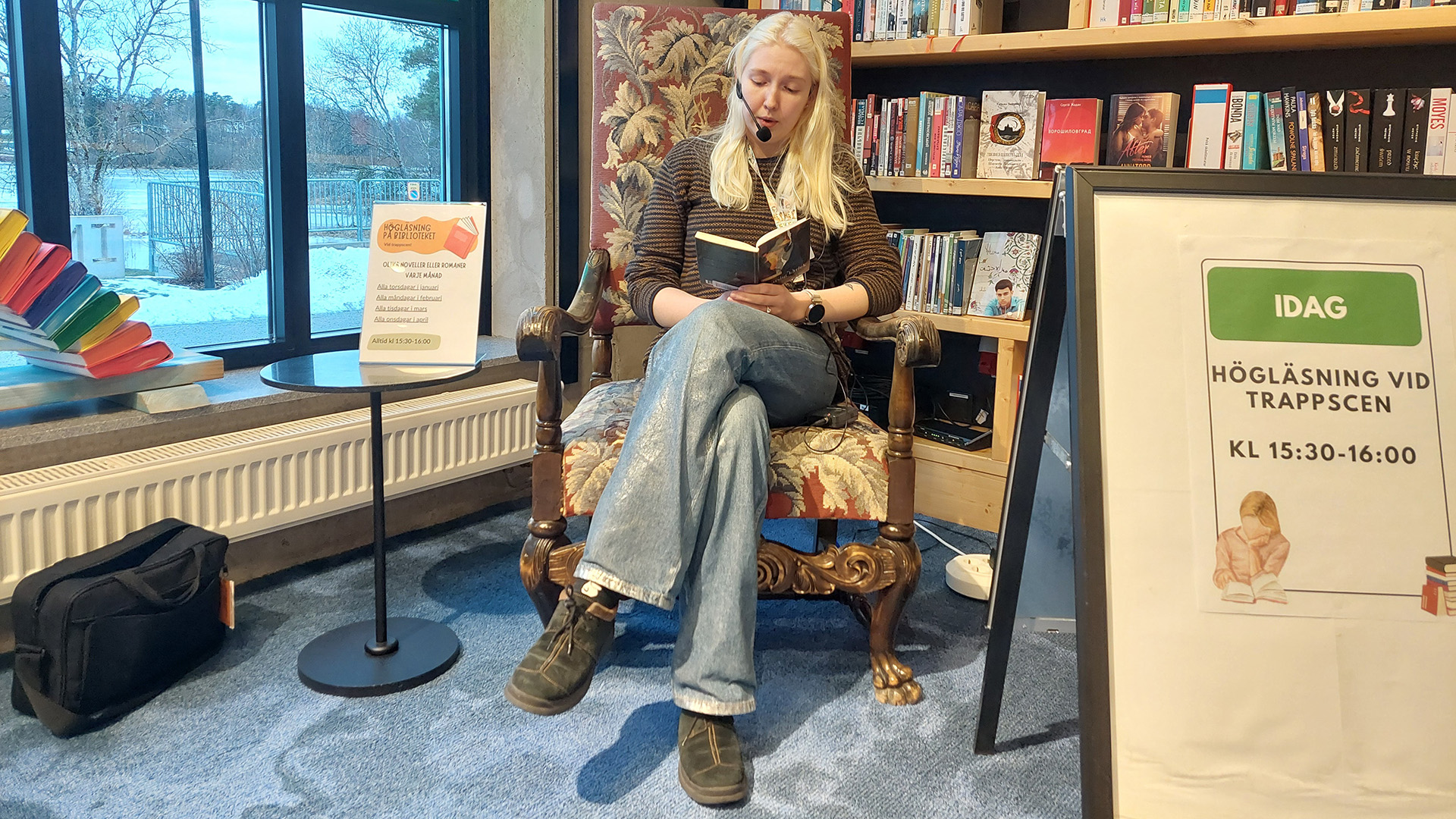 Emma Eriksson sitter i en stoppad stol med armstöd. Hon läser högt ur en bok, hon har en liten mikrofon framför munnen som är fäst vid örat. Hon har blont långt hår, är gissningsvis runt 30 år och är klädd i jeans och en randig tröja. Bakom henne finns en bokhylla och till vänster i bild finns ett fönster ut mot ett snöigt vinterlandskap. 