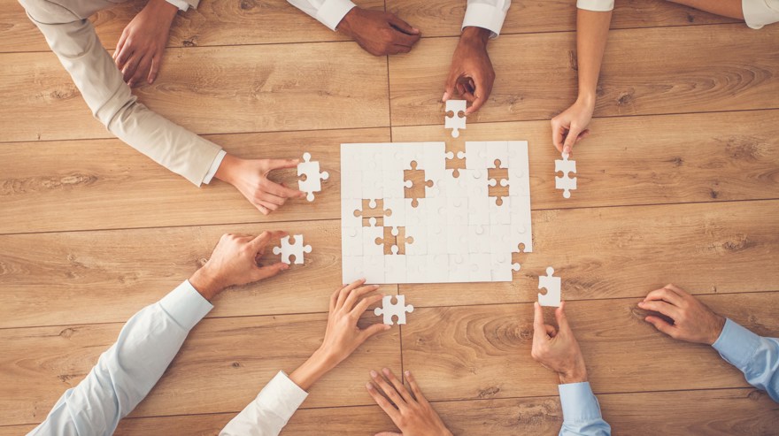 6 par armar som sträcker sig över ett bord för att lägga ett vitt pussel