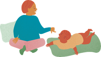 ett barn ligger på en filt på golvet, intill sitter en vuxen person och kommunicerar med händerna med barnet