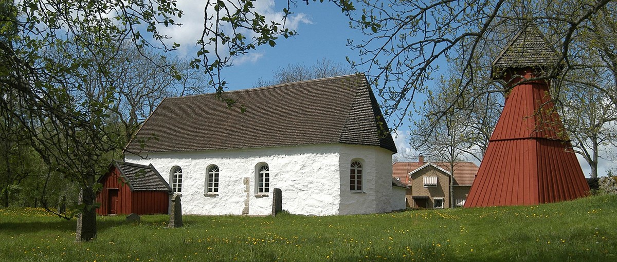 Ornunga gamla kyrka. En vit stenbyggnad med svart tak och ett rött kyrktorn i trä. 