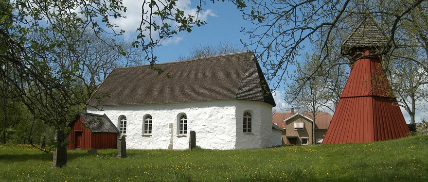 Ornunga gamla kyrka. En vit stenbyggnad med svart tak och ett rött kyrktorn i trä.