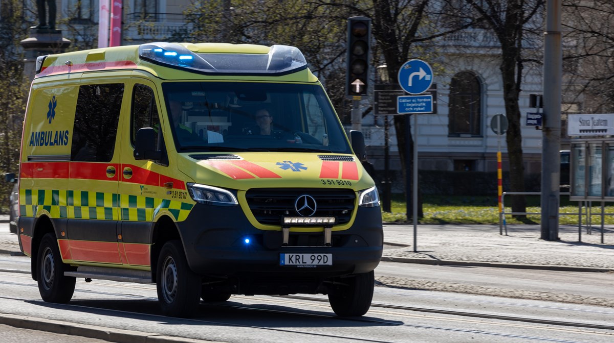 Ambulans med tända blåljus kör på gata i stad