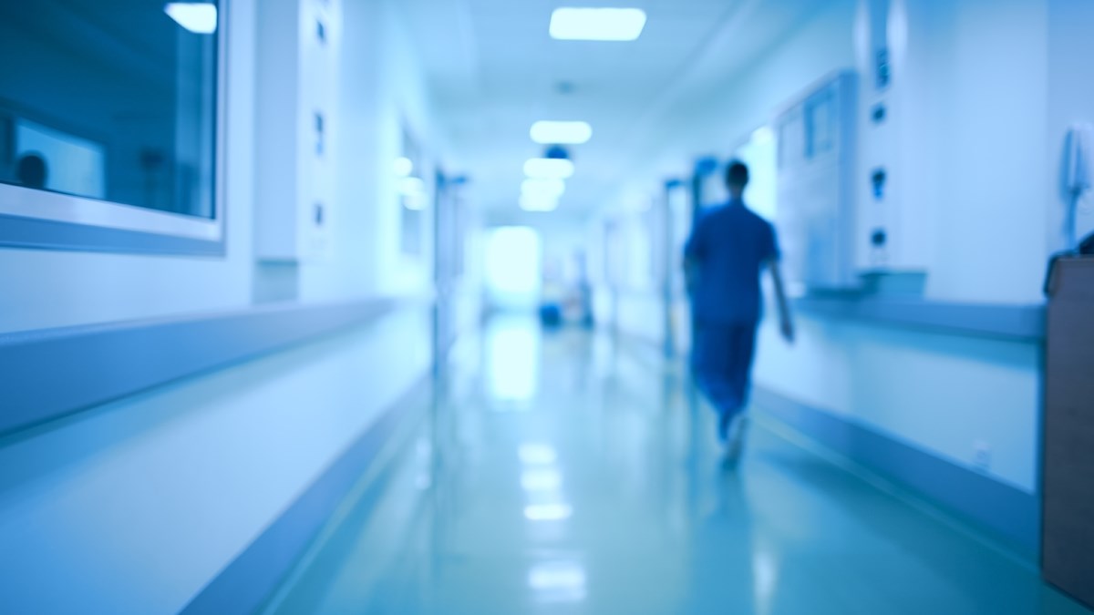 Sjukhuskorridor med en personal som går med ryggen mot kameran