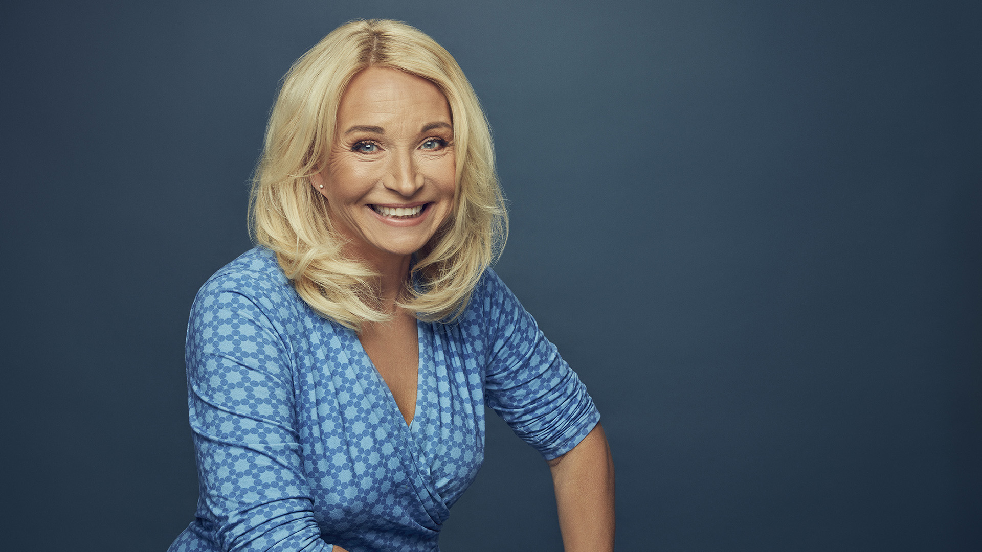 Martina Haag är i medelåldern. Hon har blont långt hår och blå ögon. Hon är klädd i en blåmönstrad omlottklänning och ler stort mot fotografen. Bilden är tagen inomhus. gissningsvis  i en fotostudio. 