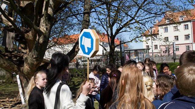 En grupp människor utomhus. En person har en blå skylt med en vit tumme på.