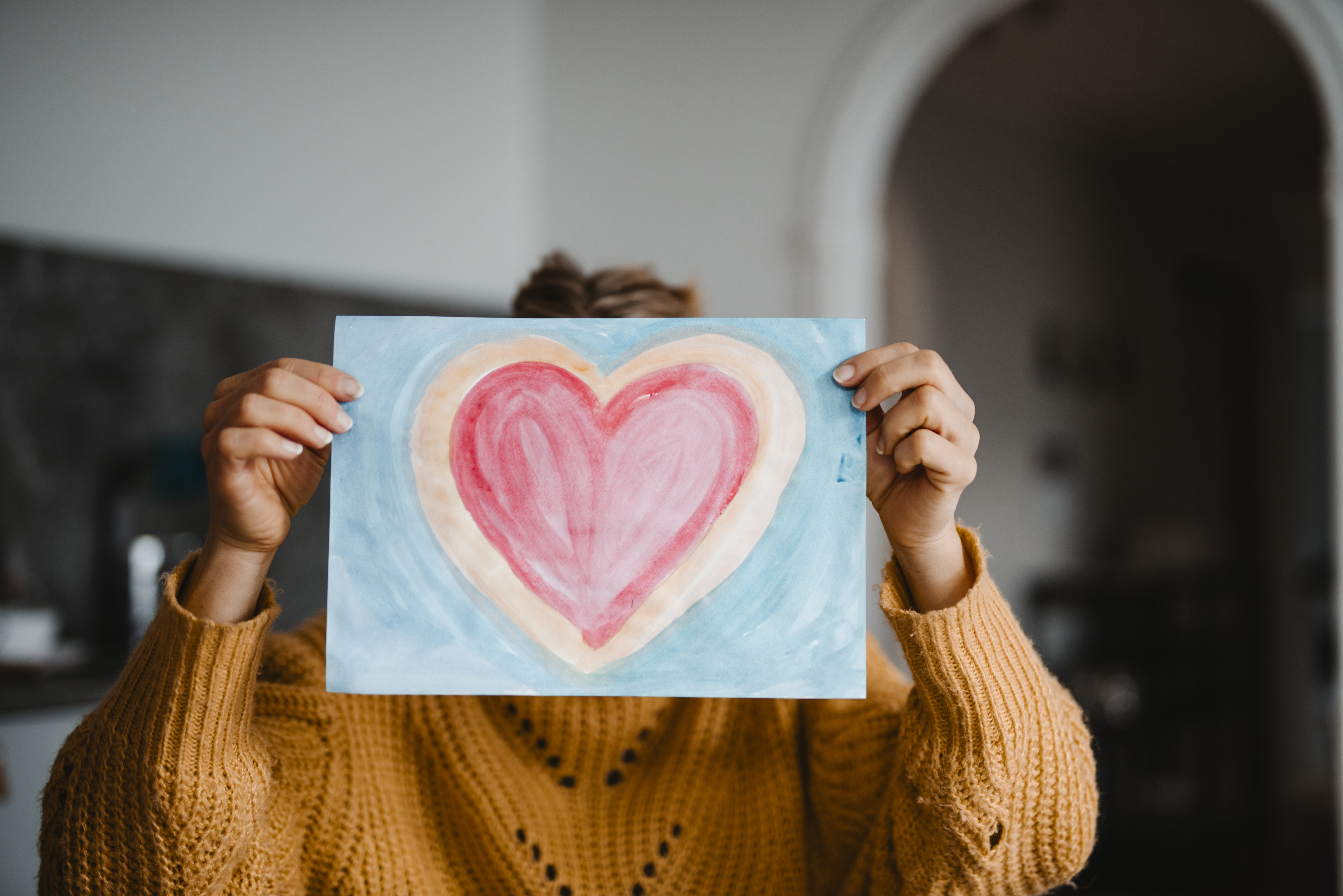 Kvinna som håller upp en bild med ett hjärta målat i vattenfärg