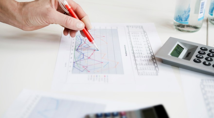 En hand som ritar kurvor på ett papper. En miniräknare intill.