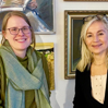 Raisa Leussu och Susanne Redebo sitter framför en vägg med tavlor. Susanne sitter till höger, hon har blont långt hår, en vit blus och en svart kofta. Raisa sitter till vänster och bär en grön tröja och en grön scarf, hon har blont uppsatt hår.