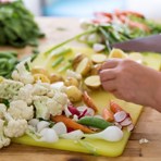 Blandade grönsaker och potatis som hackas på en gul skärbräda