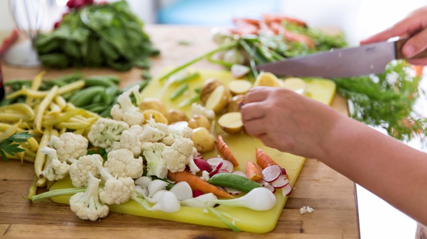 Blandade grönsaker och potatis som hackas på en gul skärbräda