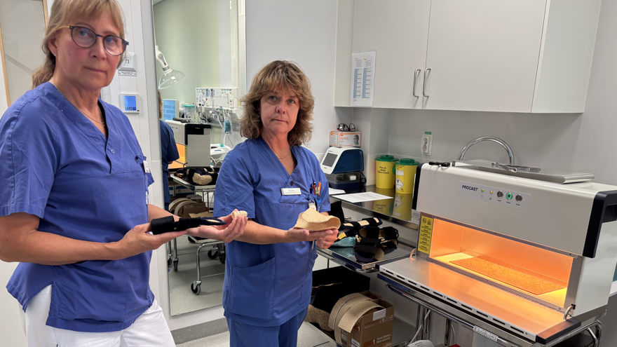 två kvinnor i blå sjukhuskläder står bredvid en ugn som används för att forma ortoser