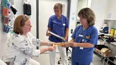 Tre kvinnor i ett vårdrum, två av dem sjukvårdsklädda. De studerar materialet som ortoserna framställs ur.