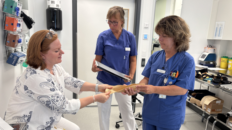 Tre kvinnor i ett vårdrum, två av dem sjukvårdsklädda. De studerar materialet som ortoserna framställs ur.