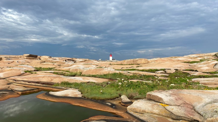 Hållö fyr med granitklippor i förgrunden mot dramatisk himmel
