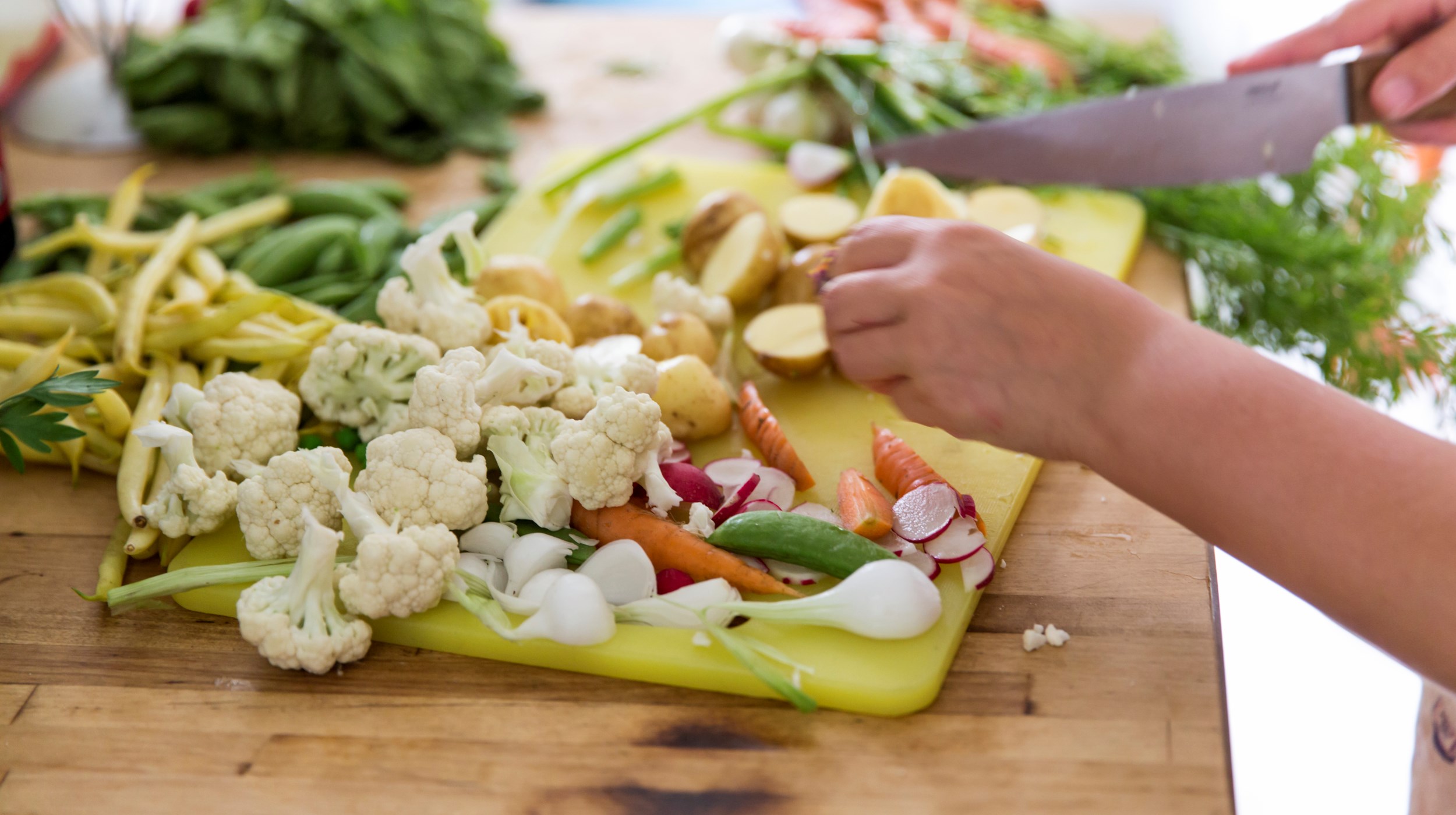 Blomkål, bönor och potatis som skärs upp på en gul skärbräda